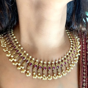 May include: A gold necklace with a teardrop design and pink gemstones. The necklace is adorned with small white pearls.