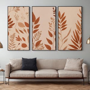 Op de afbeelding: Drie ingelijste prints met een minimalistisch ontwerp met abstracte bruine bladeren op een licht perzikkleurige achtergrond.