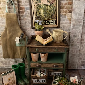 May include: A miniature garden scene with a wooden potting table, apron, and framed artwork. The artwork reads "And into the garden I go, to lose my mind and find my soul." Includes flower boxes, boots, and a watering can.