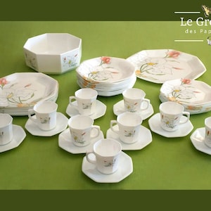 Peut inclure: Un ensemble de vaisselle octogonale blanche avec un motif floral composé de fleurs blanches, de feuilles vertes et d'accents roses. L'ensemble comprend un grand saladier, des assiettes plates, des assiettes à salade et des tasses à thé avec soucoupes. La vaisselle est étiquetée "Le Grenier des Papillons".