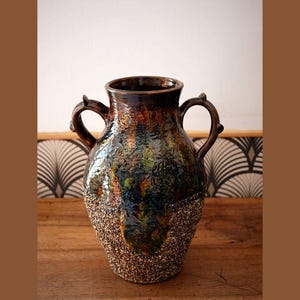 Peut inclure: Un vase en céramique brun avec une surface texturée et deux anses. Le vase a un glacis marbré brun, vert et bleu.