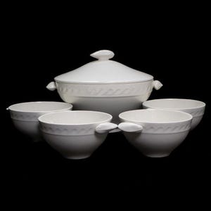Puede incluir: Un juego de servir de cerámica blanca con tapa y cuatro cuencos de sopa a juego. El juego presenta un patrón en relieve decorativo y está sobre un fondo negro. El cuenco para servir tiene dos asas.