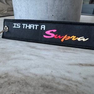 May include: Black keychain with white text that says "Is that a Supra" and a colorful Supra logo.