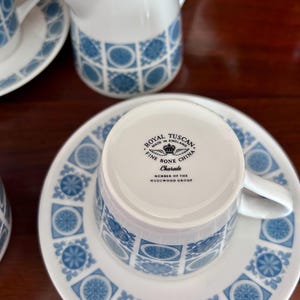 May include: A white and blue fine bone china tea set. The set includes a cup, saucer, and creamer with a repeating blue floral and geometric pattern. The cup is upside down, revealing the text "ROYAL TUSCAN FINE BONE CHINA MADE IN ENGLAND Charade MEMBER OF THE WEDGWOOD GROUP."
