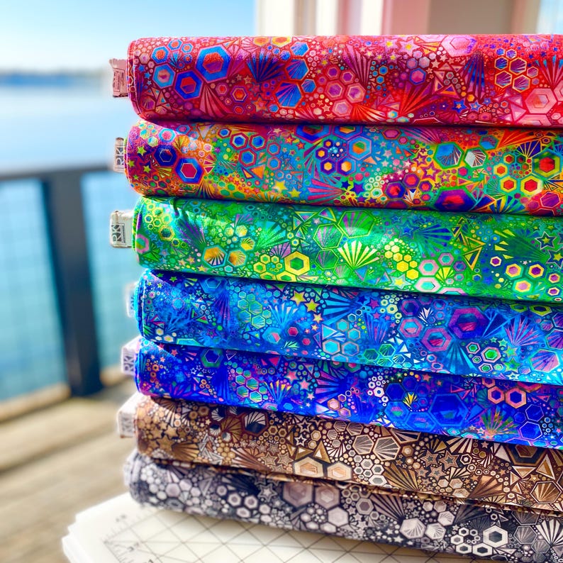 May include: A stack of colorful fabric featuring a geometric pattern with stars, hexagons, and circles. The fabric is iridescent and has a metallic sheen.