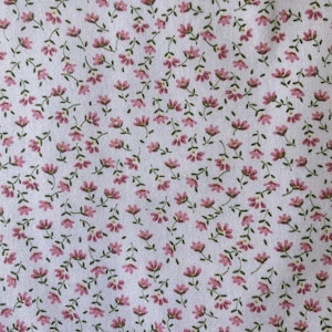 May include: White fabric with a repeating pattern of small pink flowers and green stems. The floral design is evenly distributed across the surface, creating a delicate and feminine aesthetic. The fabric appears to be cotton.