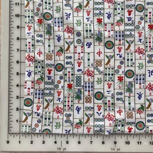 May include: White fabric with a repeating pattern of Mahjong tiles. The tiles feature various symbols, numbers, and illustrations in red, green, blue, and black. The fabric is measured with a ruler in inches.
