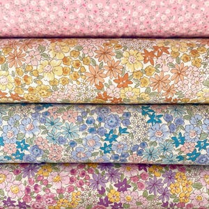 Può includere: Primo piano di quattro rotoli di tessuto floreale rosa, giallo, blu e viola. Ogni rotolo presenta un motivo floreale diverso, con fiori piccoli e grandi in vari colori. Il tessuto sembra essere cotone o un materiale simile.