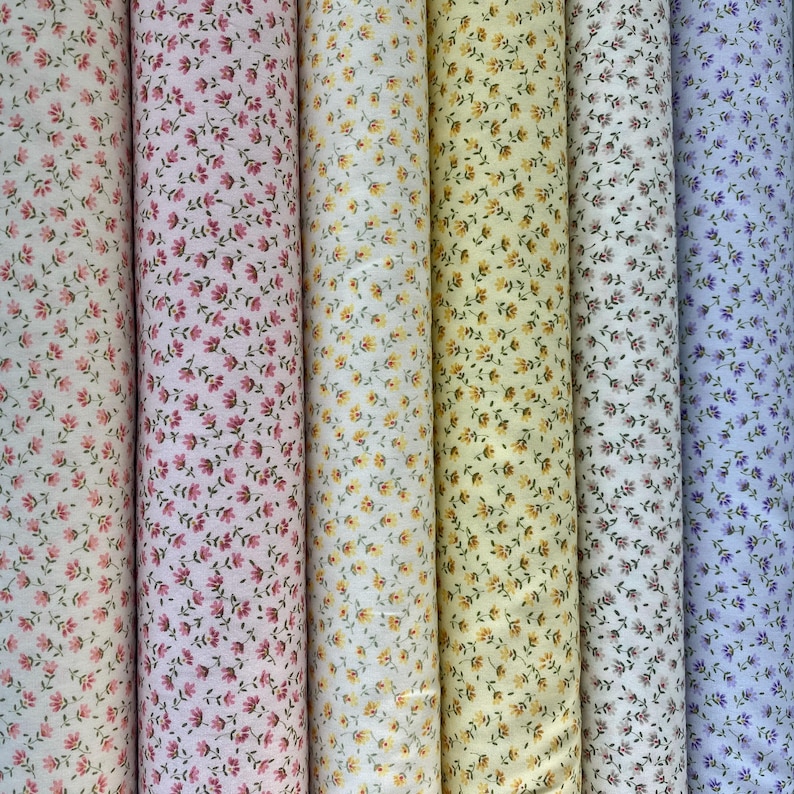 May include: A collection of fabric rolls featuring floral patterns in various colors. The fabrics display small, repeating flower designs in shades of pink, yellow, and blue on a white background. The rolls are tightly wound and vertically arranged.