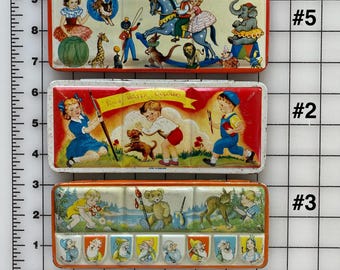 May include: Three vintage watercolor paint sets with colorful illustrations on the lids. The top set features a rocking horse, an elephant, and a giraffe. The middle set features a boy and a girl with a dog. The bottom set features a teddy bear, a deer, and a girl with a paintbrush. Each set has a different number label.