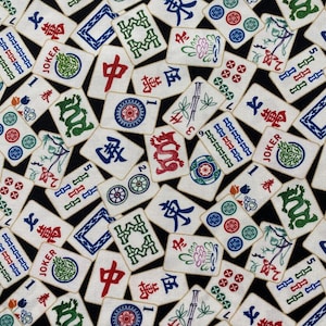 May include: A fabric with a black background covered in white Mahjong tiles. The tiles feature various symbols, numbers, and Chinese characters in red, green, blue, and black. Some tiles have the word "JOKER".