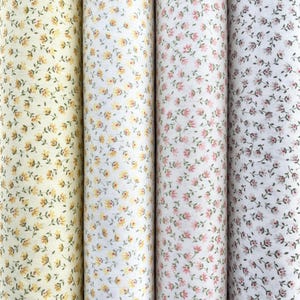 May include: Four rolls of fabric with floral patterns. The rolls display a variety of colors, including yellow, white, and pink, each adorned with small, delicate flower designs. The fabric is tightly rolled, showcasing the repeating floral patterns.