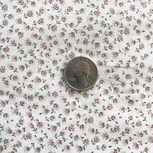 May include: Close-up of a white fabric with a delicate floral pattern. Tiny red and gray flowers with green stems are scattered across the fabric. A U.S. quarter coin is placed on the fabric for scale.