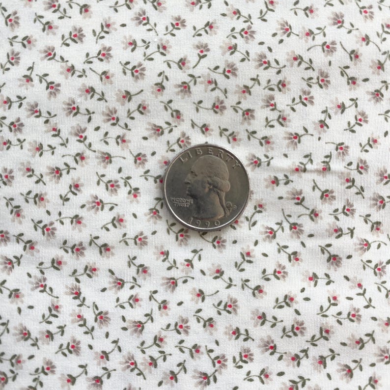 May include: Close-up of a white fabric with a delicate floral pattern. Tiny red and gray flowers with green stems are scattered across the fabric. A U.S. quarter coin is placed on the fabric for scale.