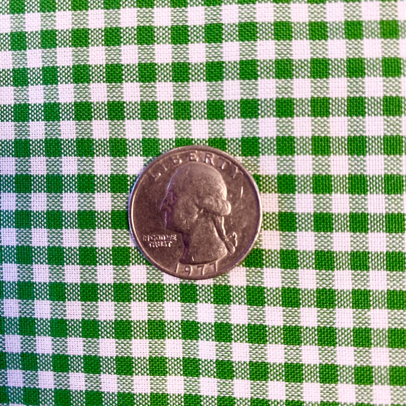 May include: A US quarter coin with a green and white gingham background. The coin is dated 1977 and features the profile of George Washington.