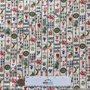 May include: Cream-colored fabric with a repeating pattern of Mahjong tiles. The tiles feature Chinese characters, numbers, and colorful illustrations of flowers, bamboo, and birds. A ruler is at the bottom.