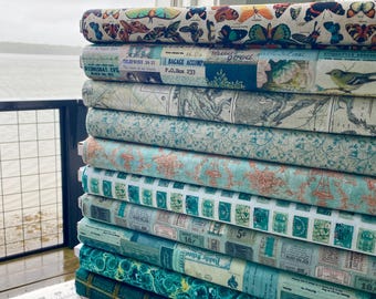 Könnte beinhalten: Ein Stapel Stoffrollen mit verschiedenen Mustern. Die oberste Rolle zeigt bunte Schmetterlinge. Andere Rollen zeigen Vintage-Prints mit Karten, Briefmarken und floralen Designs in Blau-, Grün- und Koralltönen. Die Stoffe sind in der Nähe eines Fensters gestapelt.