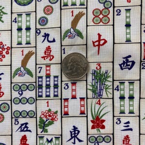 May include: Close-up of a fabric featuring a repeating pattern of Mahjong tiles. The tiles are white with various symbols, numbers, and illustrations in red, green, and blue. A U.S. quarter is included for scale.