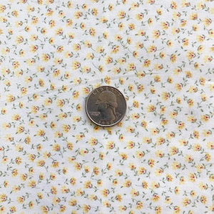 May include: Close-up of white fabric with a repeating pattern of small yellow flowers and green stems. A U.S. quarter coin is placed on the fabric, showing the year 1990. The fabric has a vintage, floral design.