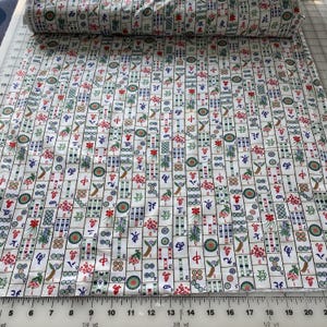 May include: White fabric roll with a repeating pattern of colorful Mahjong tiles. The tiles feature Chinese characters, floral designs, and geometric shapes in red, green, blue, and gold. The fabric is measured in yards.
