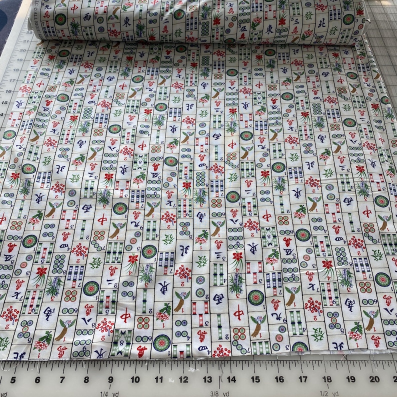 May include: White fabric roll with a repeating pattern of colorful Mahjong tiles. The tiles feature Chinese characters, floral designs, and geometric shapes in red, green, blue, and gold. The fabric is measured in yards.