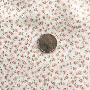May include: Close-up of a white fabric with a repeating pattern of small pink flowers and green stems. A U.S. quarter coin is placed on the fabric for scale. The floral design is delicate and detailed, creating a vintage or cottagecore aesthetic.