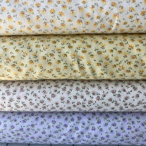 May include: Four rolls of floral fabric in various colors. The top roll is cream-colored with yellow and red flowers. The second roll is yellow with yellow flowers. The third roll is white with pink flowers. The bottom roll is lavender with purple flowers.