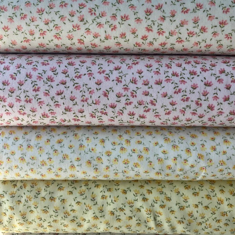 May include: Four rolls of floral fabric in varying shades. The top roll is a cream color with pink flowers and green stems. The second roll is pink with pink flowers. The third roll is white with yellow flowers. The bottom roll is yellow with yellow flowers.