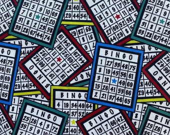 May include: A close-up of multiple colorful bingo cards with numbers and stars. The cards are arranged in a random pattern, with some overlapping. The cards are made of paper and have a white background with black numbers and red, blue, and green borders.