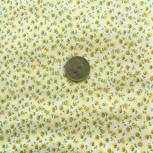 May include: Close-up of a fabric with a repeating pattern of small yellow flowers and green leaves on a cream background. A U.S. quarter coin is placed on the fabric for size reference.