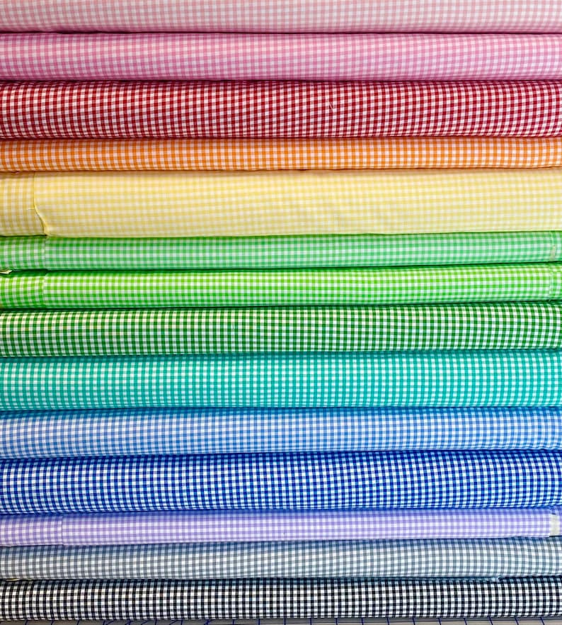 May include: A stack of colorful gingham fabric rolls in various colors, including pink, red, orange, yellow, green, blue, purple, gray, and black.