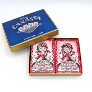 May include: Vintage Canasta card game set. The blue box with gold trim reads "Canasta" and "Unabridged Rules." The cards feature a woman in a red and white dress holding a fan of cards. The box is open, revealing the cards.