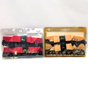 May include: Two garters in clear plastic packaging. One is red with black lace and a black ribbon that says "Yes". The other is tan with black lace and a black ribbon that says "Yes" and "No". The text "Ris-Gay Garters" is visible.