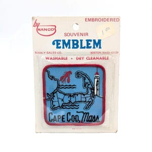 May include: Embroidered souvenir emblem of Cape Cod, Massachusetts, featuring a light blue background with a red border. The design includes a map outline, a lobster, and a lighthouse. The text "CAPE COD, Mass" is displayed.