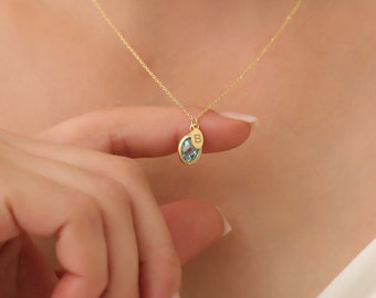 Könnte beinhalten: Eine goldene Kettenkette mit einem blauen Edelstein-Anhänger. Der Anhänger hat eine kleine goldene Scheibe mit dem eingravierten Buchstaben "B".