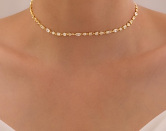 May include: A gold choker necklace with a delicate design. The necklace features small, clear gemstones in various shapes, including round, marquise, and baguette cuts. The necklace is worn around the neck.