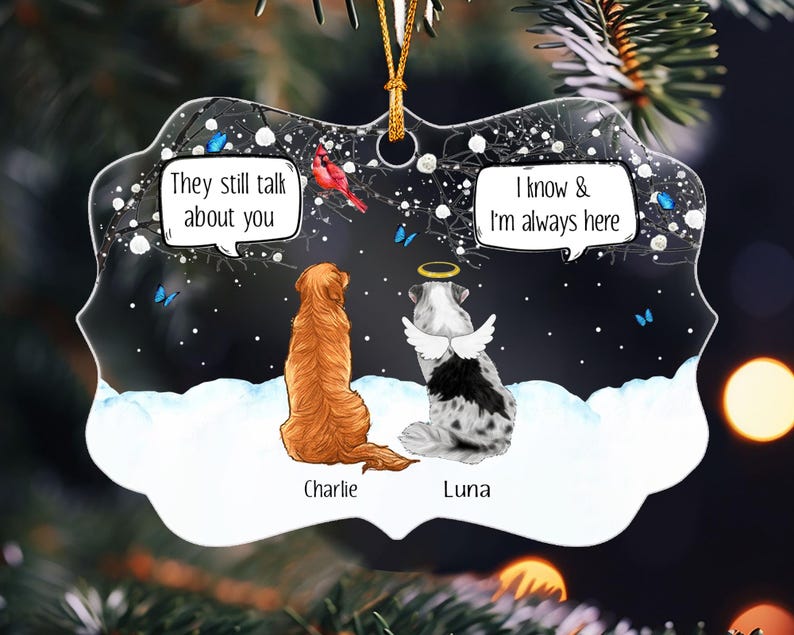 May include: A decorative ornament featuring a golden retriever named Charlie and a spotted dog named Luna with angel wings and a halo. The dogs sit in snow under a dark sky with a red cardinal and blue butterflies. Text reads: They still talk about you and I know & I'm always here.