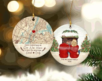 May include: Two round ceramic ornaments with gold hanging strings. One features a city map with a red heart and the text First Christmas in Our New Home, 13 West Dr, New York, Daniel and Emily. The other shows a couple by a fireplace.