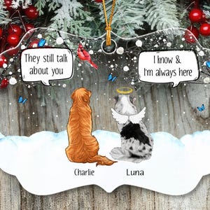May include: A clear, scalloped-edge ornament featuring a golden retriever named Charlie and a spotted dog named Luna with angel wings and a halo. Speech bubbles read, They still talk about you and I know & I'm always here, amidst snow and blue butterflies.
