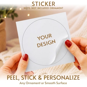 May include: A square white sticker sheet featuring a circular die-cut outline and the gold text YOUR DESIGN in the center. The sticker is partially peeled back from the backing paper. Text on the image reads STICKER, NOTE: NOT INCLUDED ORNAMENT, PEEL, STICK & PERSONALIZE, Any Ornament or Smooth Surface.