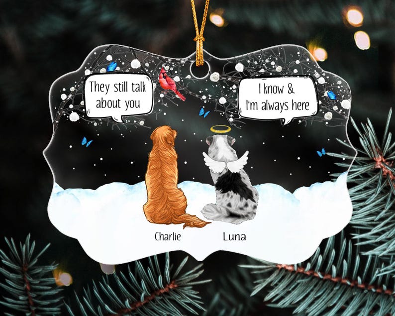 May include: A decorative ornament featuring a golden dog named Charlie and a spotted dog named Luna with angel wings and a halo. The scene shows them in snow with a red cardinal and blue butterflies. Text reads: They still talk about you and I know & I'm always here.