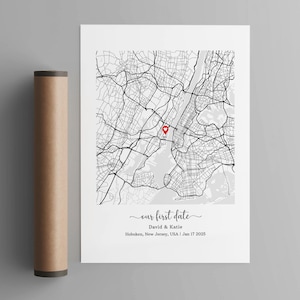 May include: A black and white map of New York City with a red heart pin marking a location. The text below the map reads "our first date", "David & Katie", "Hoboken, New Jersey, USA | Jan 17 2025".