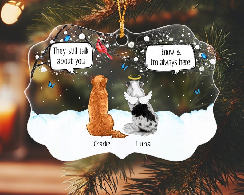 May include: A clear, scalloped-edge ornament featuring a golden retriever and a spotted dog with angel wings and a halo. The dogs sit in snow under a tree with blue butterflies and a red bird. Text bubbles read: They still talk about you and I know & I'm always here. Names Charlie and Luna are printed below.