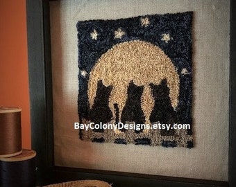 May include: A framed needlepoint artwork depicting three black cats silhouetted against a full moon with stars. The artwork is in a black frame and has a beige mat. The text "BayColonyDesigns.etsy.com" is visible in the bottom right corner.