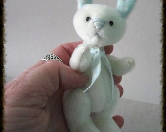 May include: A white bunny plush toy with blue and white polka dot ears and a blue ribbon around its neck. The bunny is being held by a hand. The text "E-Pattern" is in the top left corner of the image. The text "Judy Johnson BayColonyDesigns.etsy.com" is in the bottom center of the image.