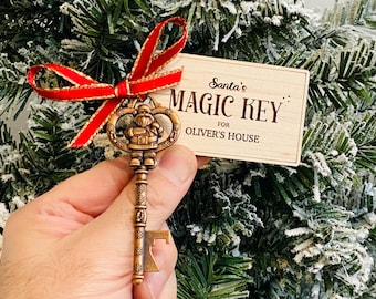 May include: A bronze-colored metal key featuring a Santa Claus figure at the top and a bottle opener at the base. A red ribbon with gold trim is tied to the key, which is attached to a rectangular wooden tag engraved with Santa's MAGIC KEY FOR OLIVER'S HOUSE.