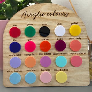 Puede incluir: Un expositor de madera con el texto "Acrylic colours" muestra una variedad de c&iacute;rculos acr&iacute;licos de colores. Los c&iacute;rculos est&aacute;n etiquetados con nombres como "rojo", "verde", "azul", "rosa", "naranja", "morado", "caramelo coral", "violeta parma", "naranja fizz", "uvas agrias", "menta verde", "sorbete de frambuesa", "azul algod&oacute;n de az&uacute;car", "azul beb&eacute;", "rosa beb&eacute;", y "bonb&oacute;n de lim&oacute;n".