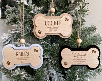 May include: Three wooden bone-shaped ornaments with personalized names and dates. The ornaments are decorated with paw prints and the text "You left pawprints in our hearts".