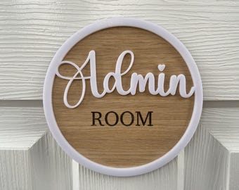 May include: A round wooden sign with a white border and the text "Admin Room" in white lettering.