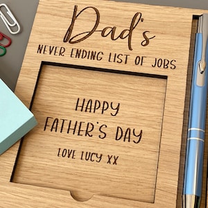 May include: Wooden desk organiser with the engraved text "Dad's Never Ending List of Jobs" and "Happy Father's Day Love Lucy XX." Includes a blue pen, a notepad, and paper clips.